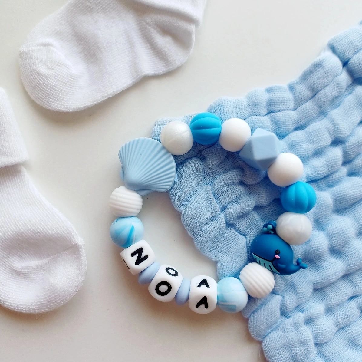 Anneau de dentition pour soulager les gencives des bébés. Cet anneau de dentition en forme de bracelet, est En silicone alimentaire sans BPA, entièrement personnalisables, perles blanches, bleues, perles du prénom et perles fantaisie en forme de baleine, et coquillage. Idéal cadeau naissance