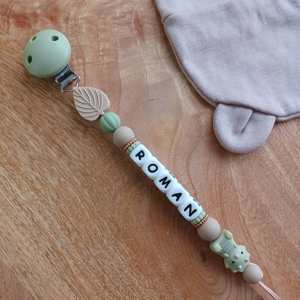 Attache tétine personnalisée bébé avec prénom, modèle dinosaure vert. Accessoire pratique et élégant, parfait comme cadeau de naissance.