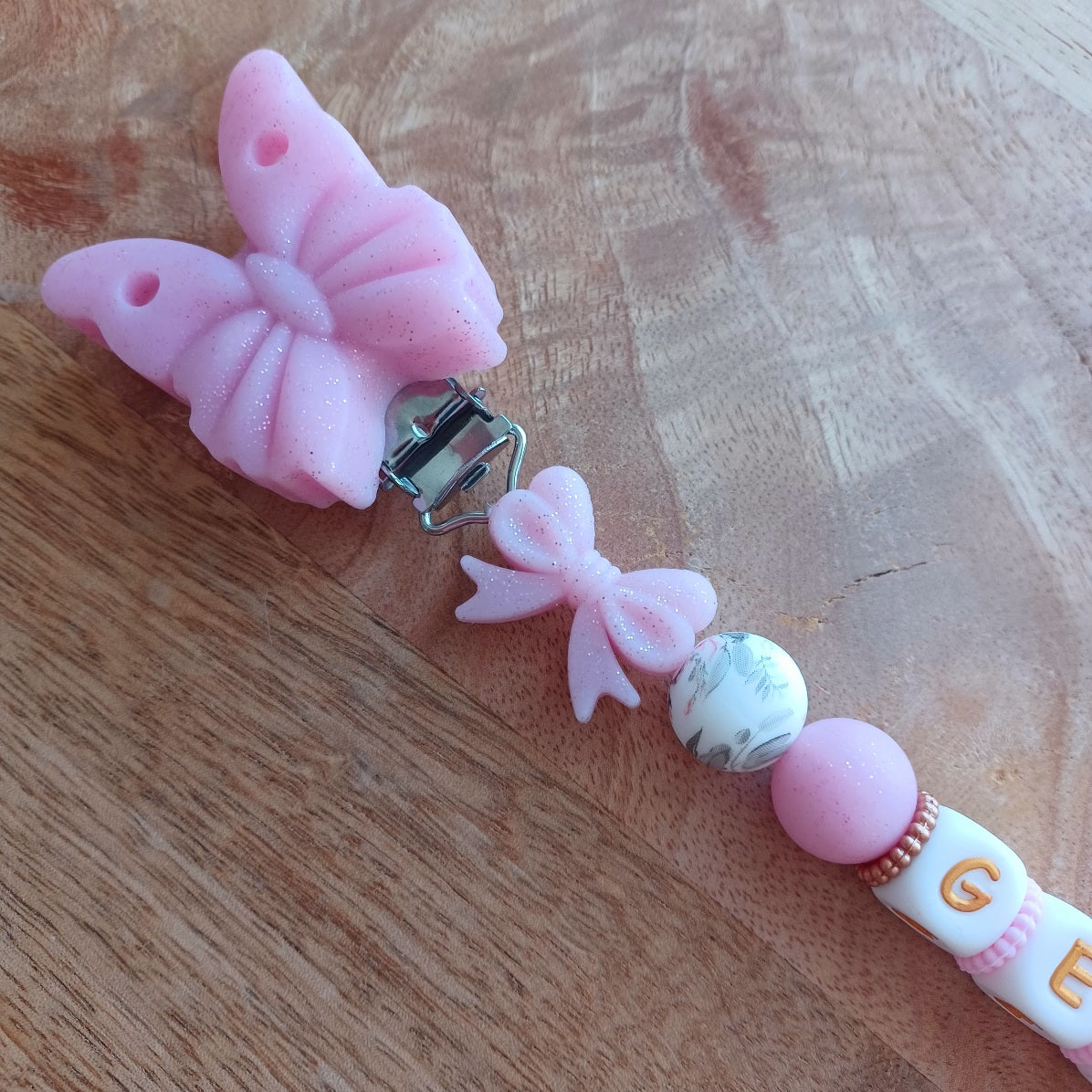 Attache tétine en silicone alimentaire sans BPA. Personnalisable avec le prénom du bébé, perles rondes, perles imprimées, perles en forme de fleurs, de noeuds, perles pailletées. Clip en silicone forme papillon. Cadeau de naissance