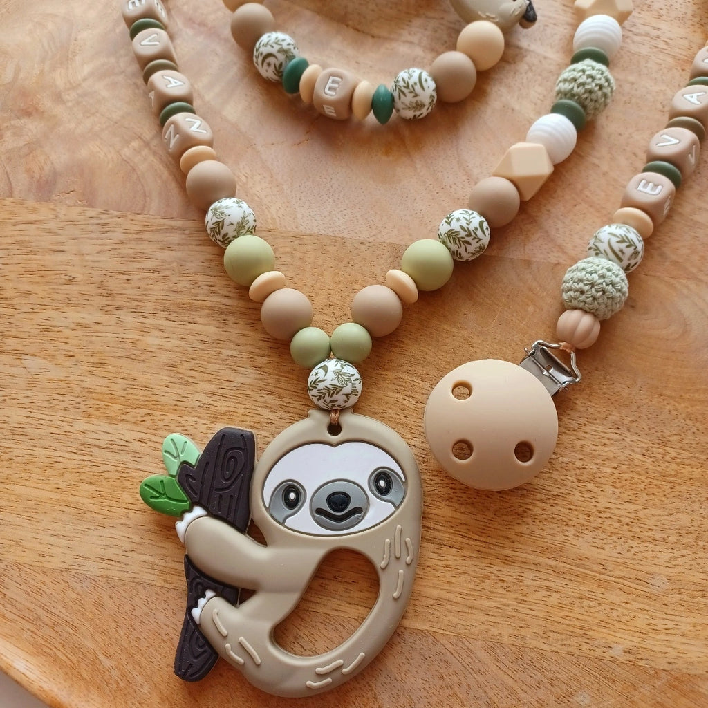 Ensemble cadeau de naissance composé de: attache tétine personnalisable, anneau de dentition, chaîne de poussette, ou et transat, aux couleurs vert, beige, taupe. Feuille et paresseux. Cadeau de naissance. 