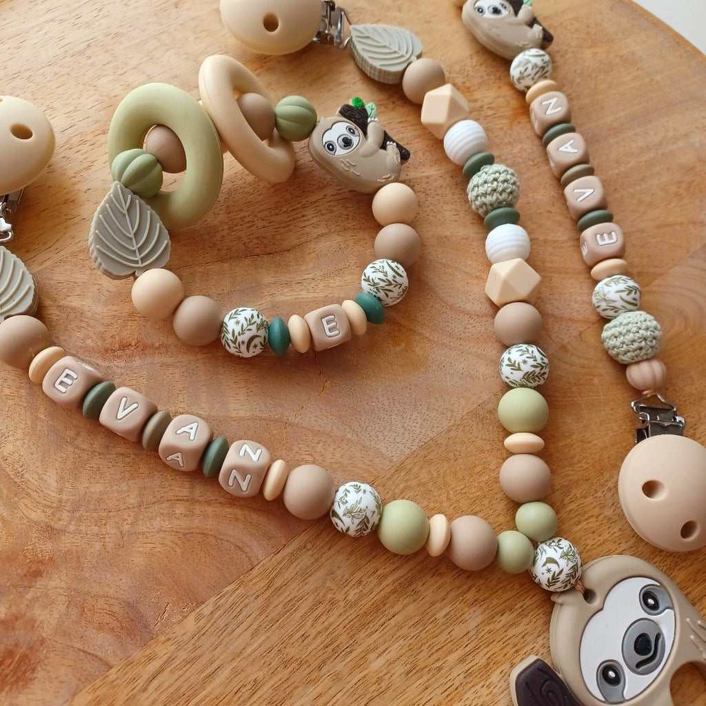 Ensemble cadeau de naissance composé de: attache tétine personnalisable, anneau de dentition, chaîne de poussette, ou et transat, aux couleurs vert, beige, taupe. Feuille et paresseux. Cadeau de naissance. 