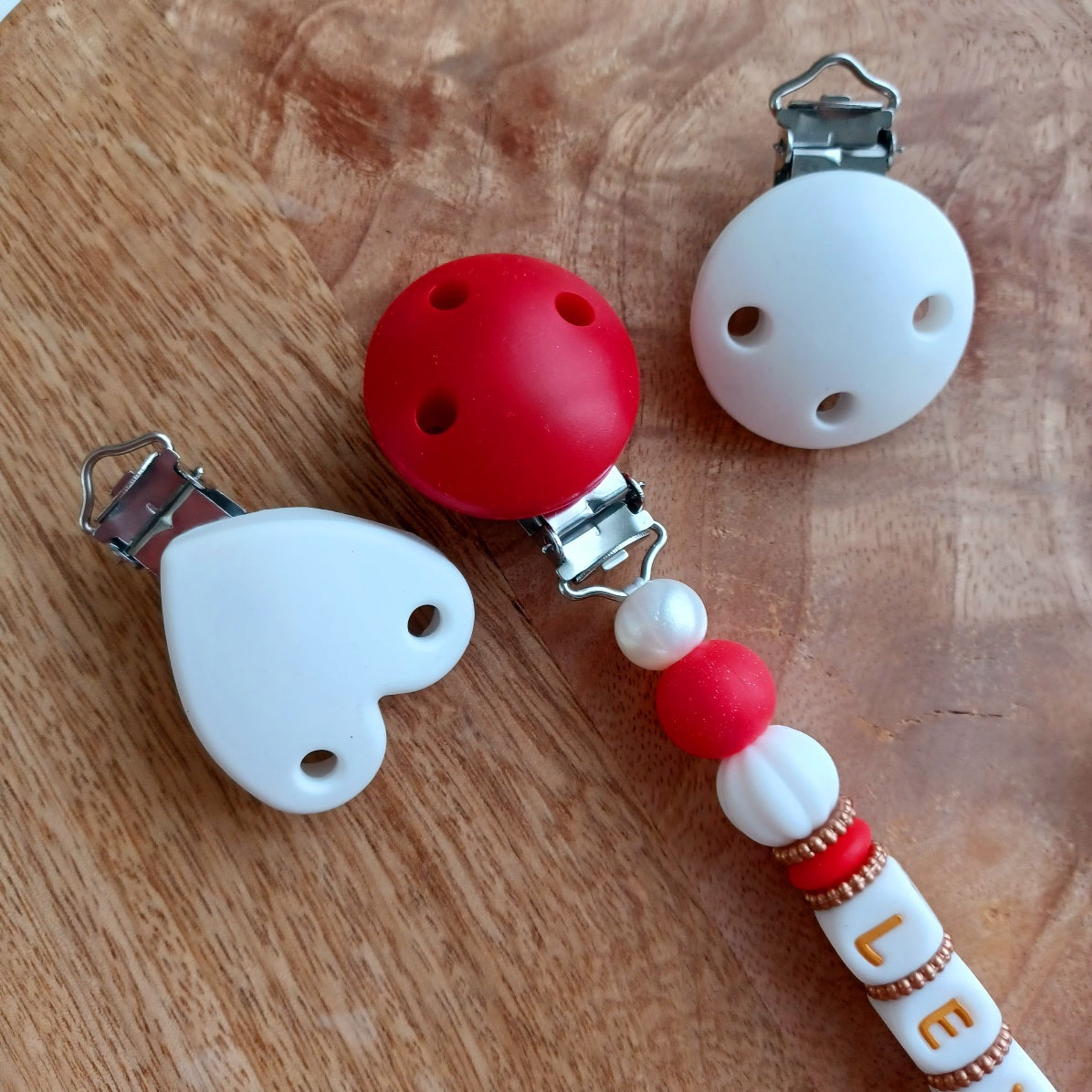 Attache tétine et anneau de dentition en silicone alimentaire sans BPA.  Clip rond en silicone et acier inoxydable, perles prénom personnalisable, papillon rouge en silicone. Anneau de dentition en taille parfaite pour les petites mains du bébé. Cadeau de naissance