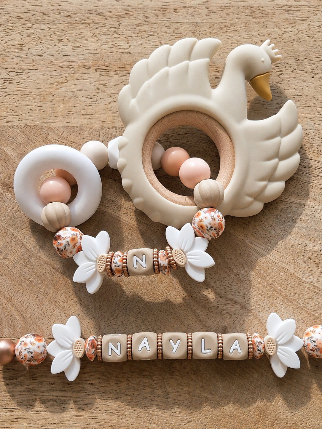 Attache tétine personnalisable avec prénom de l'enfant, en silicone alimentaire sans BPA. Clip robuste en silicone et acier inoxydable, perles imprimées, fleurs de lotus blanches. Anneau de dentition assorti.