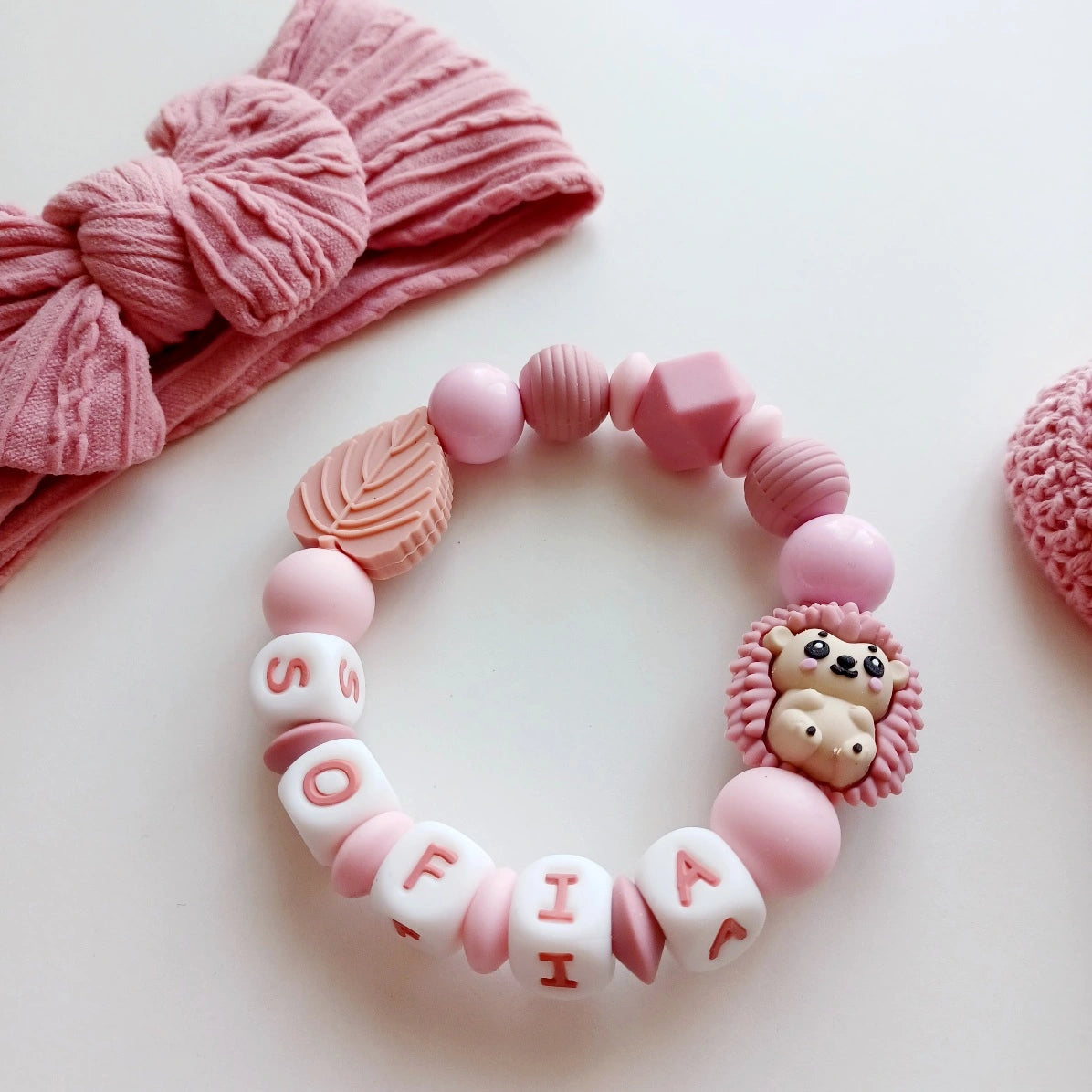 Anneau de dentition pour soulager les gencives des bébés. Cet anneau de dentition en forme de bracelet, est En silicone alimentaire sans BPA, entièrement personnalisables, perles rose, rose poudré, vieux rose, perles du prénom et perles fantaisie en forme d'hérison, et feuille. Idéal cadeau naissance