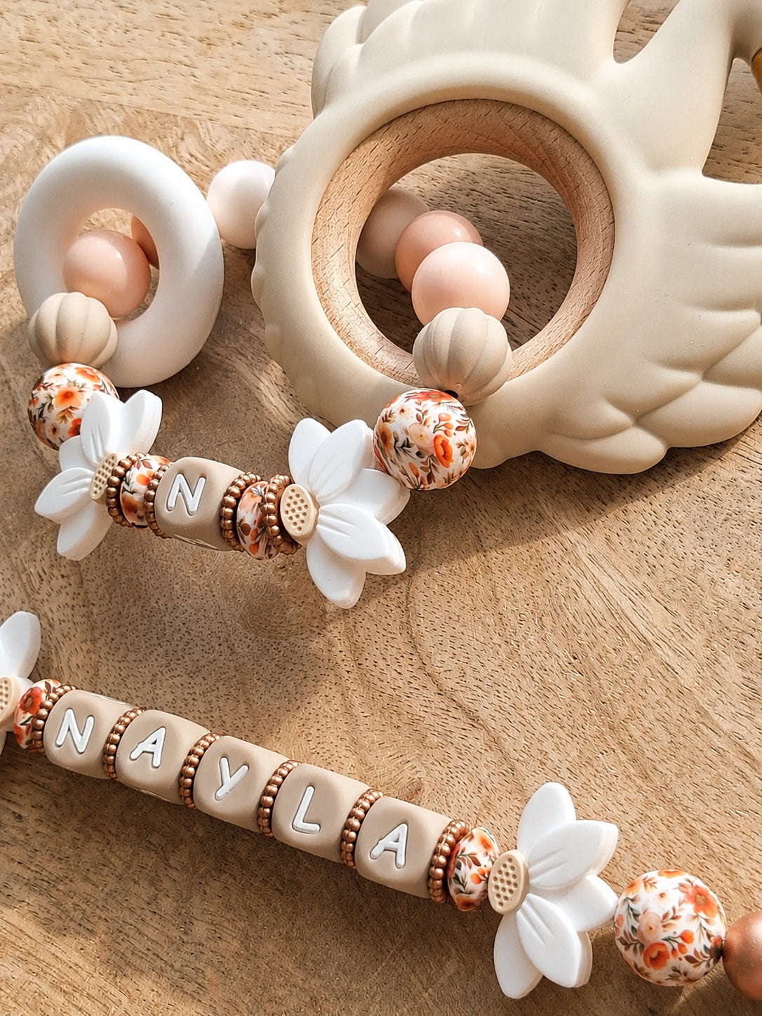 Attache tétine personnalisable avec prénom de l'enfant, en silicone alimentaire sans BPA. Clip robuste en silicone et acier inoxydable, perles imprimées, fleurs de lotus blanches. Anneau de dentition assorti.