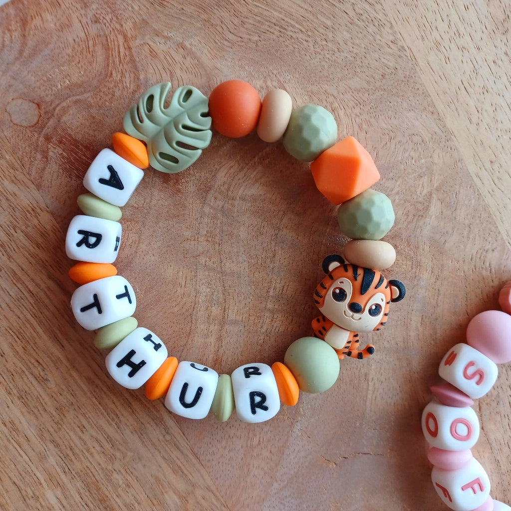 Anneau de dentition pour soulager les gencives des bébés. Cet anneau de dentition en forme de bracelet, est En silicone alimentaire sans BPA, entièrement personnalisables, perles vertes, oranges, perles du prénom et perles fantaisie en forme de tigre et feuille. Idéal cadeau naissance