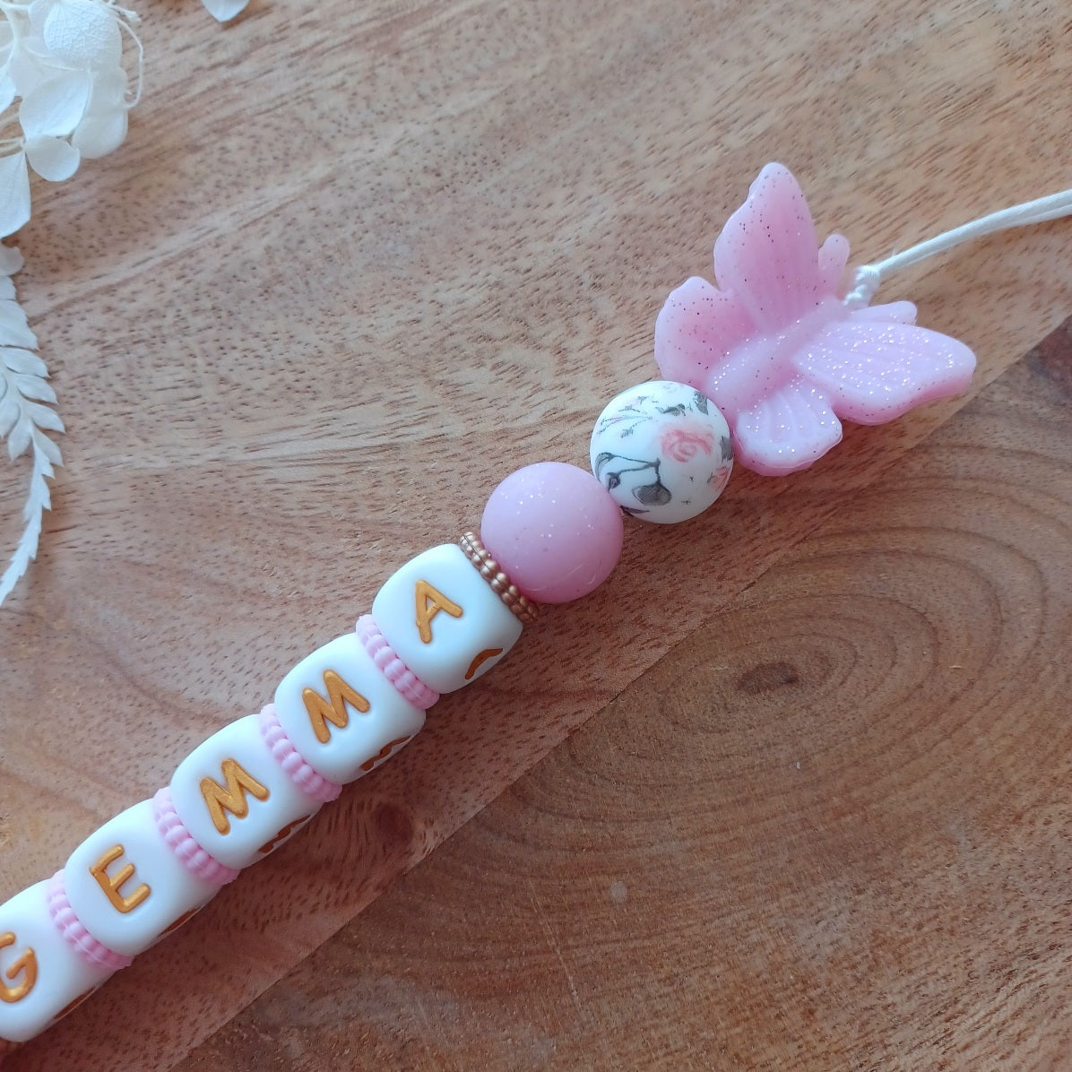 Attache tétine en silicone alimentaire sans BPA. Personnalisable avec le prénom du bébé, perles rondes, perles imprimées, perles en forme de fleurs, de noeuds, perles pailletées. Clip en silicone forme papillon. Cadeau de naissance