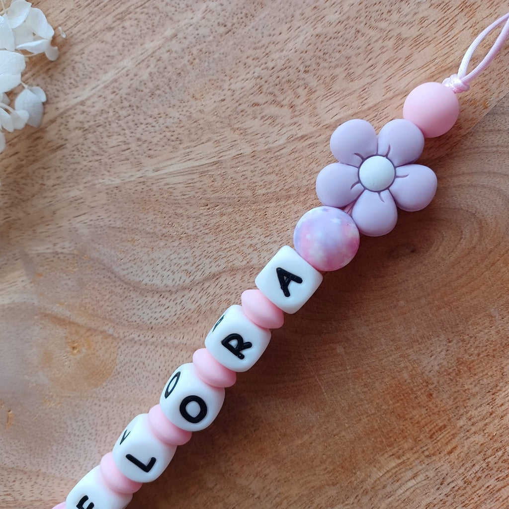 Attache tetine personnalisable, avec prénom du bébé ou enfant. Clip forme de fleur en silicone et acier inoxydable, perles du prénom en blanc et noir, perles rondes en lilas et rose pastel, perles de fleur . Cadeau de naissance