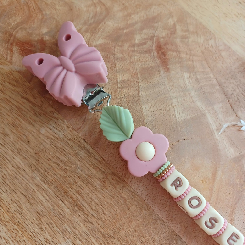 Attache tétine en silicone alimentaire sans BPA. Personnalisable avec le prénom du bébé, perles rondes, perles imprimées, perles en forme de fleurs, de noeuds, perles pailletées. Clip en silicone forme papillon. Cadeau de naissance