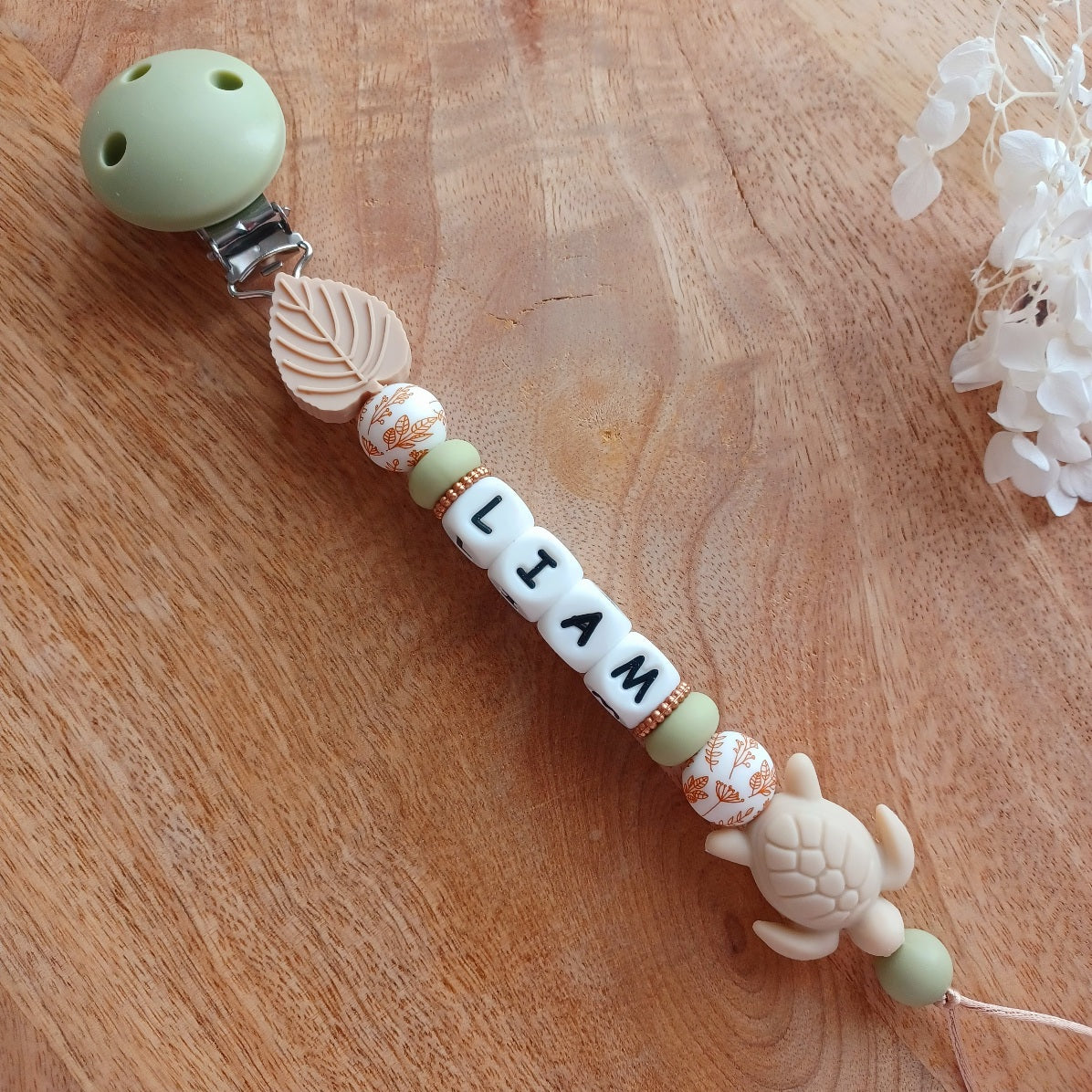 Attache tétine et anneau de dentition personnalisable en silicone alimentaire sans BPA, pour les bébés. Personnalisation avec prénom, perles ronds, fleuries, et perles ludiques en forme de feuilles et petits animaux (tortues, oiseaux, lions, safari, savane.