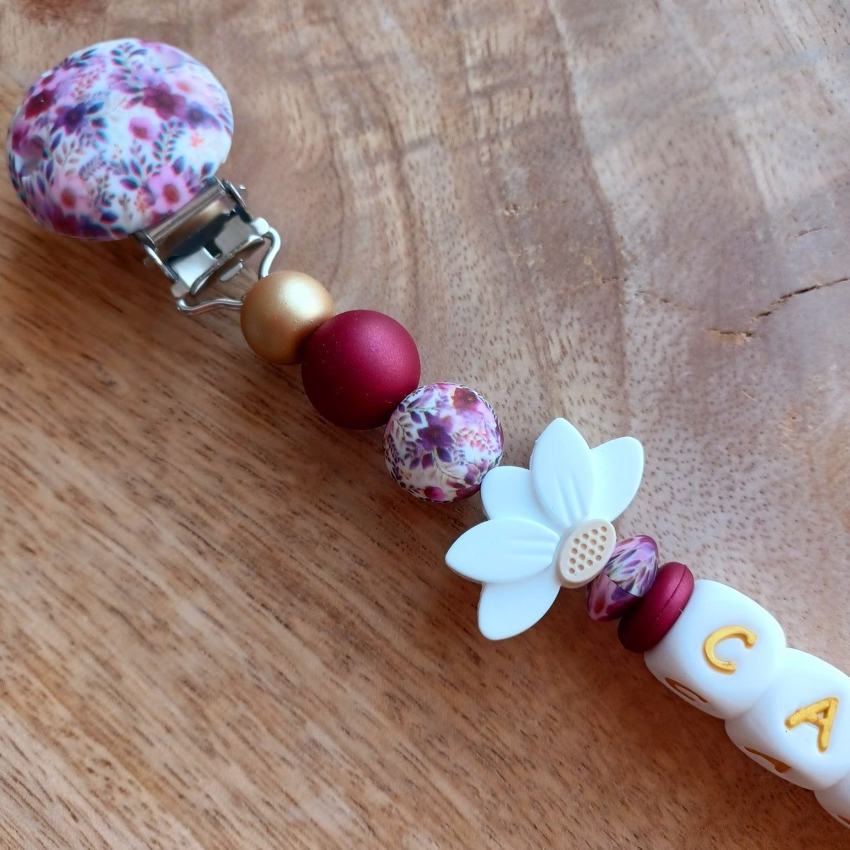 Attache tétine personnalisée en silicone avec prénom Cazu et fleurs blanches. Une attache tétine en silicone alimentaire sans bpa. Un anneau de dentition en silicone alimentaire, et cygne 