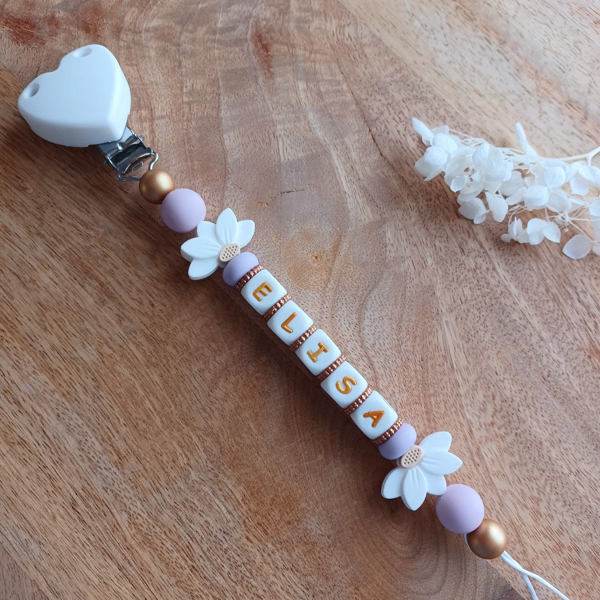 Attache tetine personnalisable, avec prénom du bébé ou enfant. Clip forme de coeur en silicone et acier inoxydable, perles du prénom en blanc et doré, perles rondes en lilas, perles de fleur de lotus. Cadeau de naissance