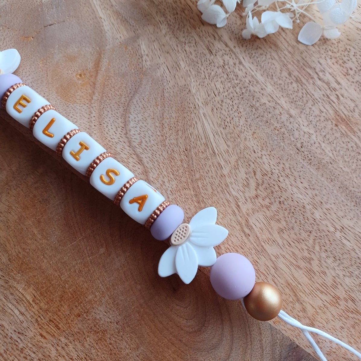 Attache tetine personnalisable, avec prénom du bébé ou enfant. Clip forme de coeur en silicone et acier inoxydable, perles du prénom en blanc et doré, perles rondes en lilas, perles de fleur de lotus. Cadeau de naissance