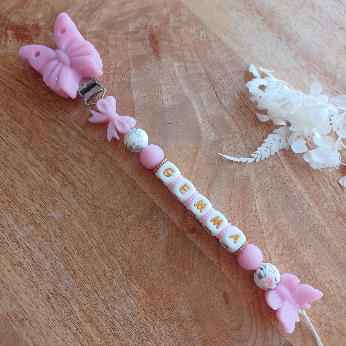 Attache tétine en silicone alimentaire sans BPA. Personnalisable avec le prénom du bébé, perles rondes, perles imprimées, perles en forme de fleurs, de noeuds, perles pailletées. Clip en silicone forme papillon. Cadeau de naissance