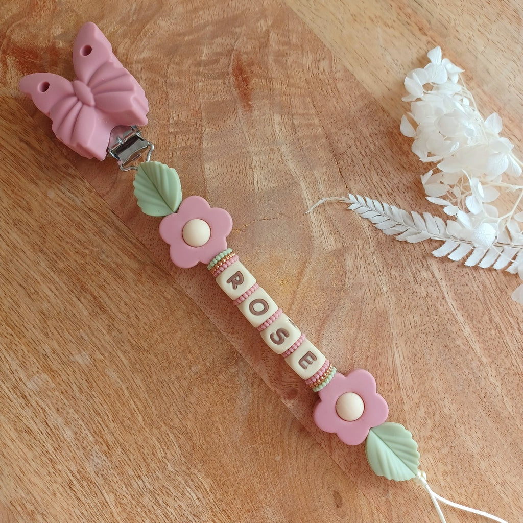 Attache tétine en silicone alimentaire sans BPA. Personnalisable avec le prénom du bébé, perles rondes, perles imprimées, perles en forme de fleurs, de noeuds, perles pailletées. Clip en silicone forme papillon. Cadeau de naissance