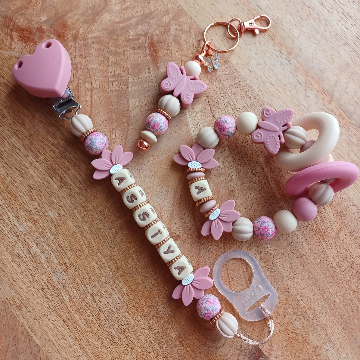 Attache tétine personnalisable avec le prénom de l'enfant, accompagné de son anneau de dentition assorti, en silicone alimentaire sans BPA. Aux couleurs vieux rose et beige