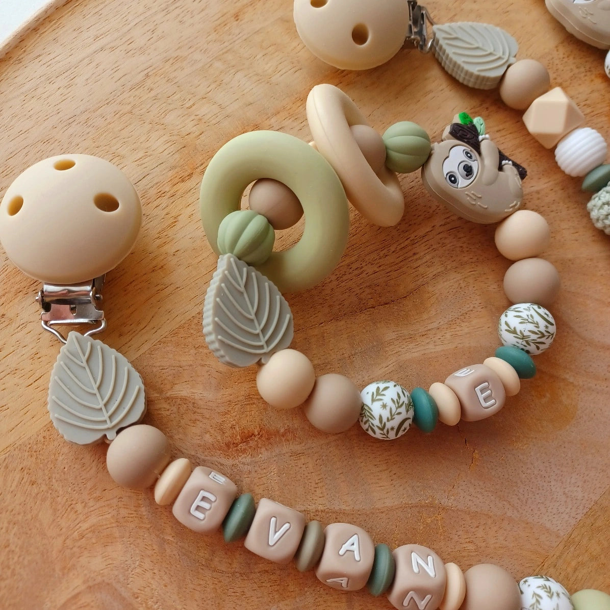 Ensemble cadeau de naissance composé de: attache tétine personnalisable, anneau de dentition, chaîne de poussette, ou et transat, aux couleurs vert, beige, taupe. Feuille et paresseux. Cadeau de naissance. 