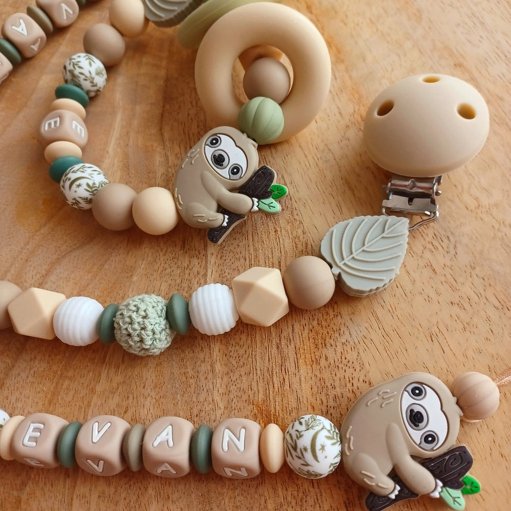 Ensemble cadeau de naissance composé de: attache tétine personnalisable, anneau de dentition, chaîne de poussette, ou et transat, aux couleurs vert, beige, taupe. Feuille et paresseux. Cadeau de naissance. 